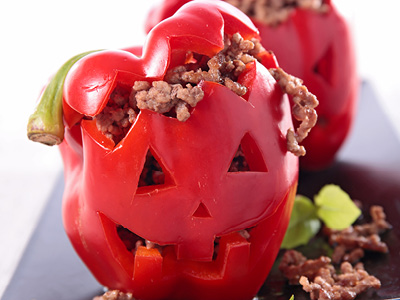 Red peppers  cut out like a jack-o-lantern stuffed with ground beef mixture on a black plate